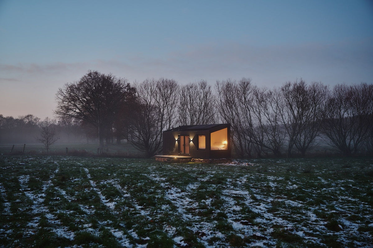 Lit Raus cabin in a snowy field at dusk